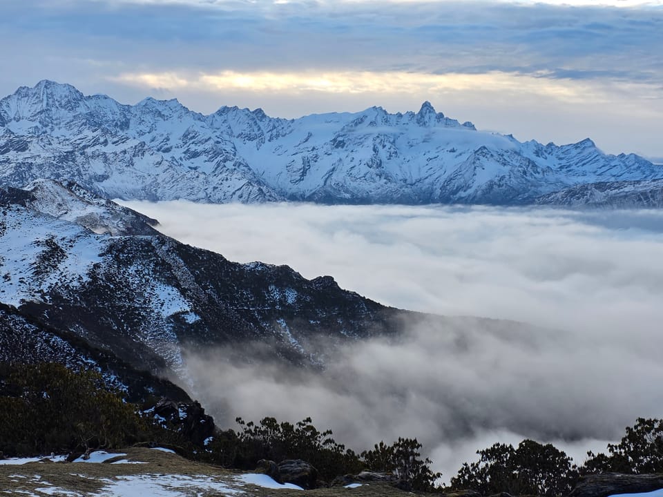 A wide snow-covered mountain range rising above a valley of cloud